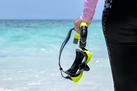Woman on the beach and Swimsuit a pink.Holding Goggles,scuba diving Black-yellow.Happy smile.The backdrop is sky and sea.の写真素材