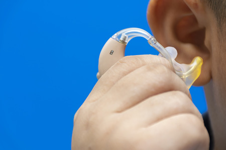 Hand that is catching hearing aid, To wear. It is his first device, Blue background. To live in...