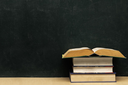 Four books stacked, the topmost book opened. Put on the table and the back is a blackboard.
