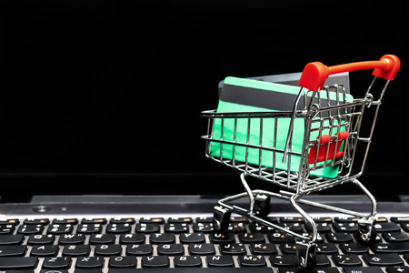 Online Business is popular in the present day, the computer is located on a desk, a trolley with two credit cards.の写真素材