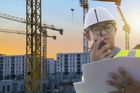 Leadership of Construction work needs certainty,precision,Engineers are in control Using radio  communication tools and see the blueprints,Heavy construction yellow crane for heavy lifting.の写真素材