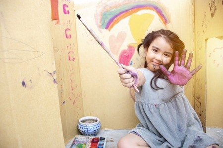 Girl Hand is holding paintbrush to draw on paper,Art lesson ,adorable little girl smiling happily while enjoying art and craft lesson in Paper Box House.の写真素材