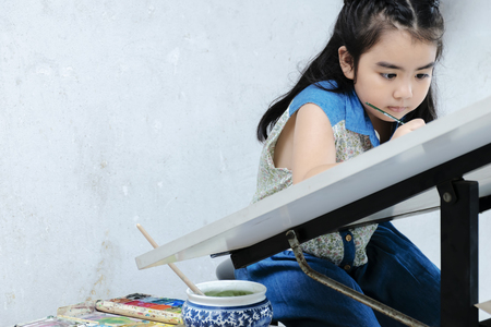 Girl Hand is holding paintbrush to draw on paper,Art lesson ,adorable little girl smiling happily while enjoying art and craft lesson in school working.の写真素材