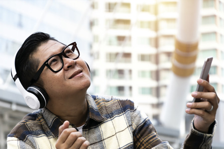 Men are sitting happily listening to music.Using headphones connected to  a smartphone.の写真素材