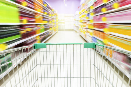 Supermarket aisle with empty green shopping cart. The image is animated with zoom to make it look interesting.の写真素材