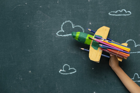 Back to school concept with Paper rocket made from pencils over chalkboard background,
The hand of the child is holding Paper rocket.の写真素材