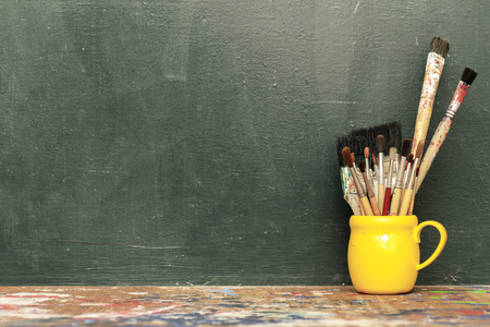 Brushes of various sizes and styles. Put it in a yellow tile glass. Placed on a wooden table with a messy color. The backdrop is black paper.の写真素材