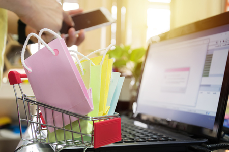 Colorful paper shopping bags in a trolley. concept online shopping. Online Shopping Website on Laptop. Easy E-commerce Website Shop by Smartphone, Using Smartphone Shopping.の写真素材