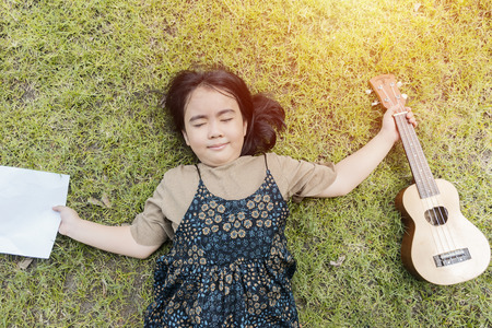 Happy Girl with Music concept. She was lying on the grass. Holding an Acullete and Note music.の写真素材