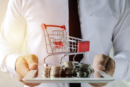 Business online concept. Businessmen are holding a tabloid with lots of coins and trolley. Easy E-commerce Website Online Shopping on Laptop.の写真素材