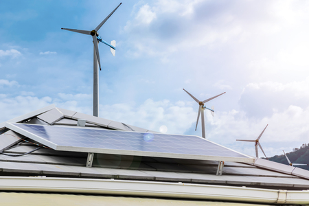 Electricity is essential to life. Pure energy is a very valuable alternative energy. Roofing house with solar panel, Photovoltaic cell. The background is wind turbines for electricity.の写真素材