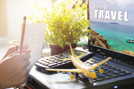 Travel Planning Concepts. Checking out the passbook and checking the web site,Time to travel on laptop. Hand holding a pencil. Calculator, airplane model, visual element. copy space.の写真素材