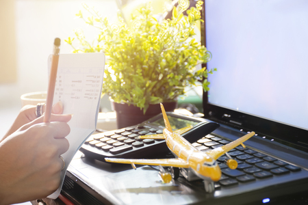 Travel Planning Concepts. Checking out the passbook and checking the web site,Using a laptop. Hand holding a pencil. Calculator, airplane model, visual element. copy space.の写真素材