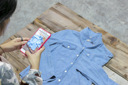 Selling Online concept. Women taking photo to shirts with cell telephone or smartphone digital camera for Post to sell Online on the Internet .の写真素材
