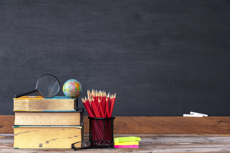 Back to school concept. Education is important for everyone to succeed. Front side the book is stacked and has a pencil case,Magnifying glass, globe, glasses,The background is blackboard.の写真素材