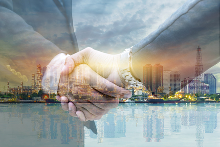 Businessmen are shaking hands for business venture and Marketing to invest in energy. The background is a large oil refinery. The work is ongoing.の写真素材