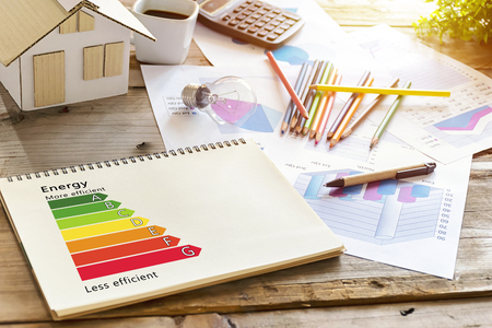 Concept of ecological and bio energetic house.Energy class.The desk has its place,house models,crayons,bulbs,coffee cup,calculator,Statistical documents,Detail of house efficiency rating on notebooks.の写真素材