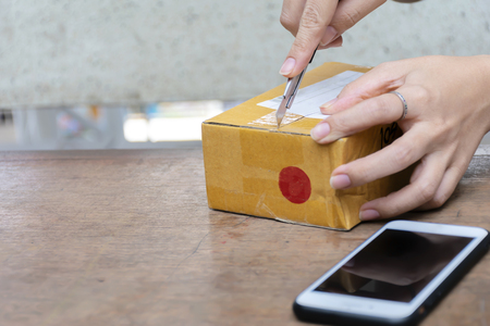 Shopping Online concept. Women who are unpacking products ordered on the Internet. The product was boxed as well. Prevent damage to objects. Open with a cutter and a smartphone is placed.の写真素材