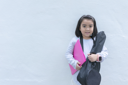 The girl is ambition to be a musician. Begin to study Ukulele, holding a ukulele and a note book. Asian girl standing in the background with a white wall.の写真素材
