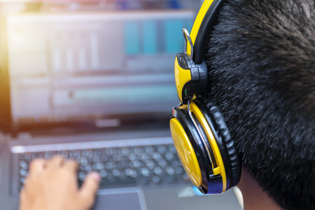 video editing, computer laptops and headphones. with laptop. Professional editor adding special effects or color grading footage. Back view of young man using computer software and wearing headphones.の写真素材