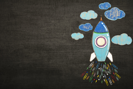 Back to school concept. Great success must start with learning. A beautifully colored paper rocket rests on a blackboard. Pin and paper clip made to jet engine. copy space.の写真素材