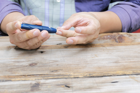Man taking blood sample with lancet pen. Diabetes concept. Medicine, Diabetes, Glycemia, Health care and people - close up using lancelet on finger to checking blood sugar level by Glucose meter.の写真素材