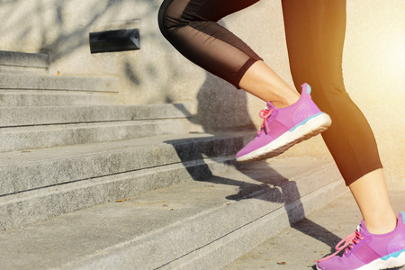 Fitness sport concept, woman in fashion sportswear doing fitness exercise in the city street over gray concrete background. Outdoor sports clothing and shoes, young woman running up the stairs.の写真素材