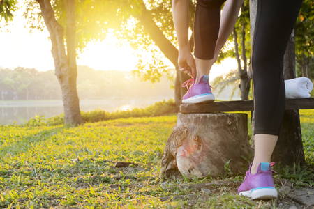 Fitness sport woman in fashion sportswear doing fitness exercise in the public park. The background is a large pond. Outdoor sports clothing and shoes, young woman runner tying shoelaces.の写真素材