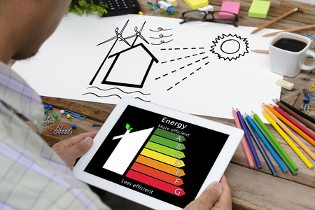 Man holding digital tablet and looking at house efficiency rating. Detail of house efficiency rating on digital tablet screen. Concept of ecological and bio energetic house. Energy class.の写真素材