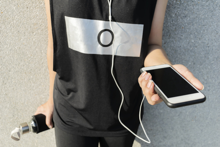 Relaxing muscles from exercise. By listening to music in the smartphone. Wear a black sportswear. Blank screen to enter text. And hold a bottle of water.の写真素材
