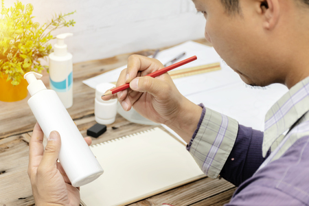 Designers are designing products.Packaging that can put cream, lotion, and liquid.The hand holding the product and holding a pencil, Desk area with equipment.Must use creative ideas to create works.の写真素材