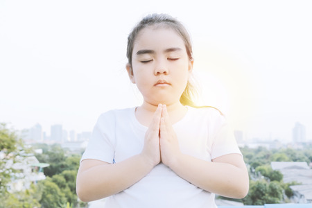 Praying to God with faith in that. Both exist and do not exist. It is a matter of faith and experience. Asian girl wearing a white shirt, High-angle house background.の写真素材
