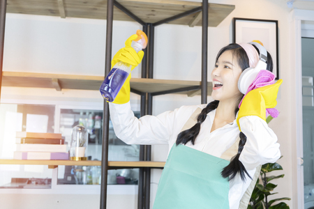 Happy to work concept. A beautiful woman who is cleaning her house by Cleaning fluid and soft cloth. She is happy to work by listening to music by wearing headphones.の写真素材