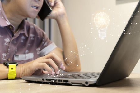 Innovation concept. Businessmen are using laptops, hands are touching the Touchpad. He is using the phone to communicate. Graphic created as a light bulb.の写真素材