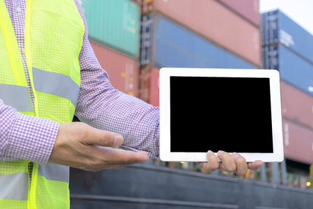 Logistic concept. Engineering is holding a tablet. Free space to be able to enter text or images to create an advertising media. The background is a large cargo carrying container.の写真素材