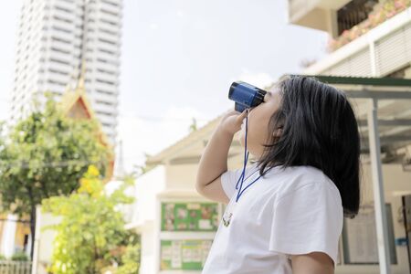 Girls wearing white shirts are using blue binoculars. The background is a tall building.の写真素材