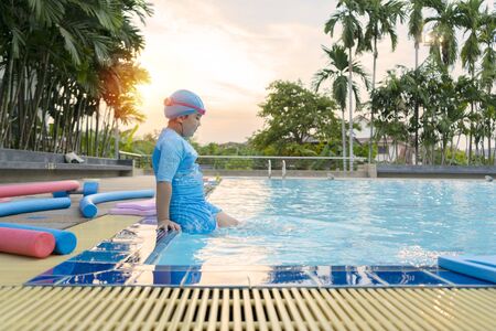 Happy girl sitting around swimming pool and looking,  Swimming pool class learning to swim. Warming the body by using the legs to hit the water.の写真素材