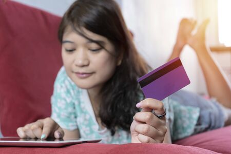 Buy online concept. Women are using tablets to shop online. By paying by credit card for convenience and speed, She lay on a red sofa at home.の写真素材