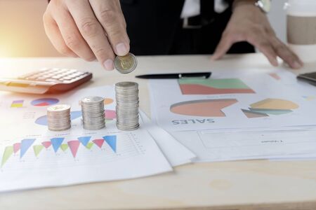 Business investment concepts. Businessmen who are holding coins to put on coins, Work desk with documents on investment graphs, calculators.の写真素材