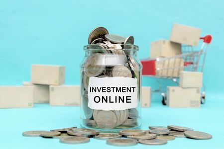 Online business investment, A glass jar with coins filled out. The background is a shopping cart with lots of parcel boxes.の写真素材