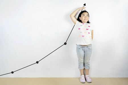 The cute Asian girl looks like she is measuring the height. She has a continuous development and a good trend as well. The continuous up arrow is a comparison.の写真素材
