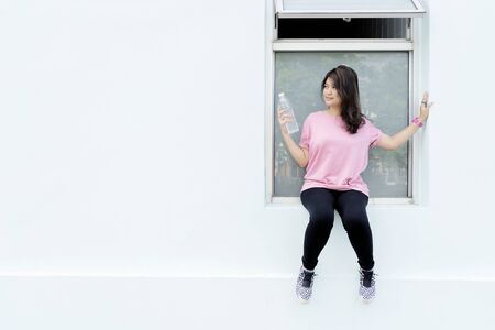 Fitness concept. Women who exercise a lot, she is standing tired. She is sitting, resting and drinking pure water to balance the body.の写真素材