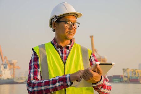 Engineers use tablets concept. Industrial Engineer in Hard Hat Wearing Safety Jacket Uses Touchscreen Tablet Computer. He Works at the Heavy Industry Manufacturing.の写真素材