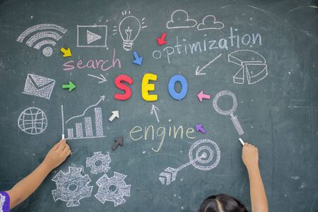 SEO Search Engine Optimization concept. The Plasticine molding that was molded into the SEO alphabet, The background is a blackboard. People are drawing symbols related to the search.の写真素材
