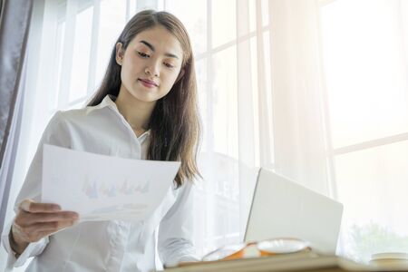 Business woman wearing suit, looking, holding documents in hands compatible with laptops. In the area by the window, of charming, sexy, caucasian, modern.の写真素材