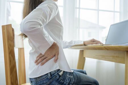 Young businesswoman feels uncomfortable sitting in office chair, woman massaging her back suffering from discomfort ache pain, incorrect posture from long sedentary work and lower backache conceptの写真素材