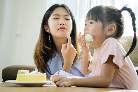 Asian sisters and sisters, they are happily eating cakes. The place in the living room has a sofa and a central table.の写真素材