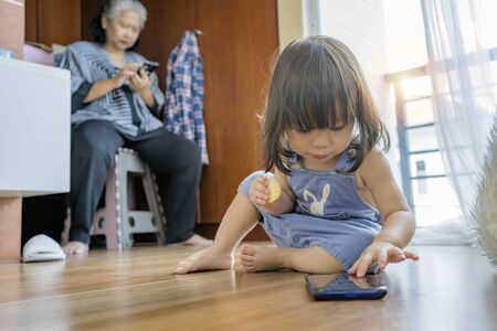 Granddaughter and grandmother both are using a smartphone at home. Future family conditions that use technology Innovation in daily life.の写真素材