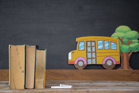 Back to school concept. Textbooks, books on the table, a chalkboard background and a tree on the school bus.の写真素材