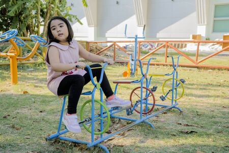 An Asian girl is playing on a playground. She is riding a bicycle alone.の写真素材